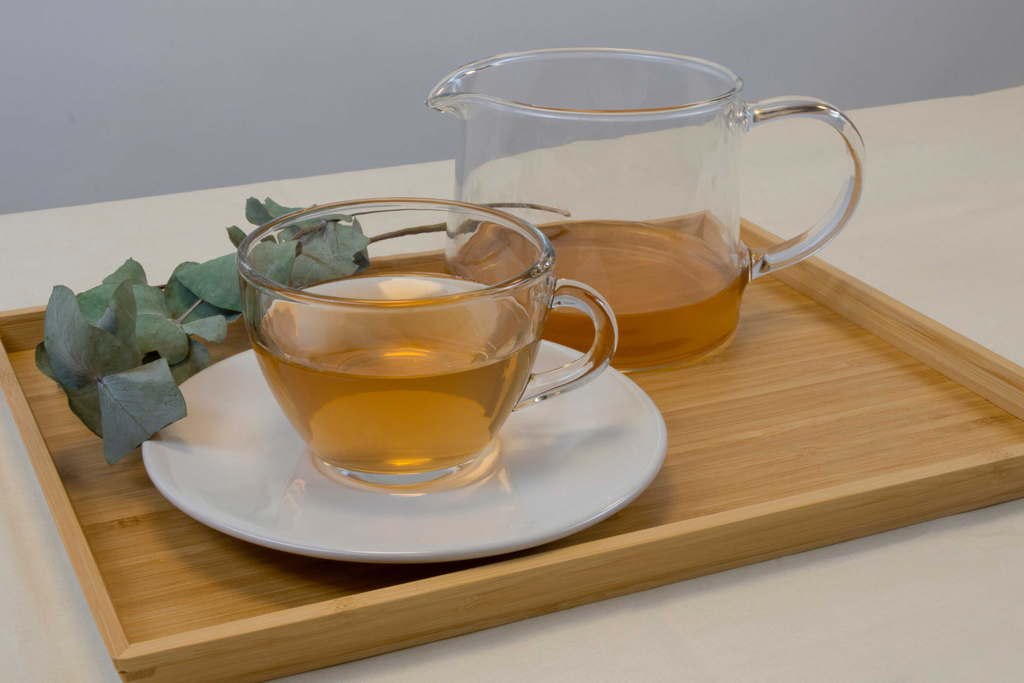 wood tray with tea pot and tea cup filled with organic green tea.